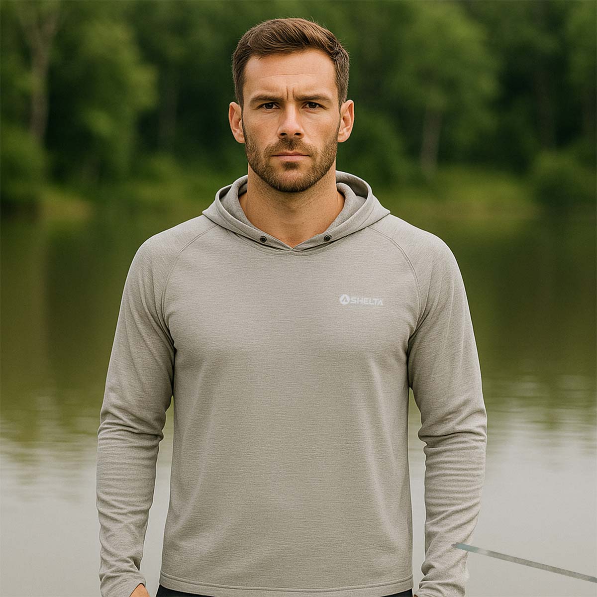 Man wearing a gray hoodie with a brand logo standing by a body of water.