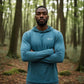 Man wearing a blue hoodie with a brand logo in a forest setting