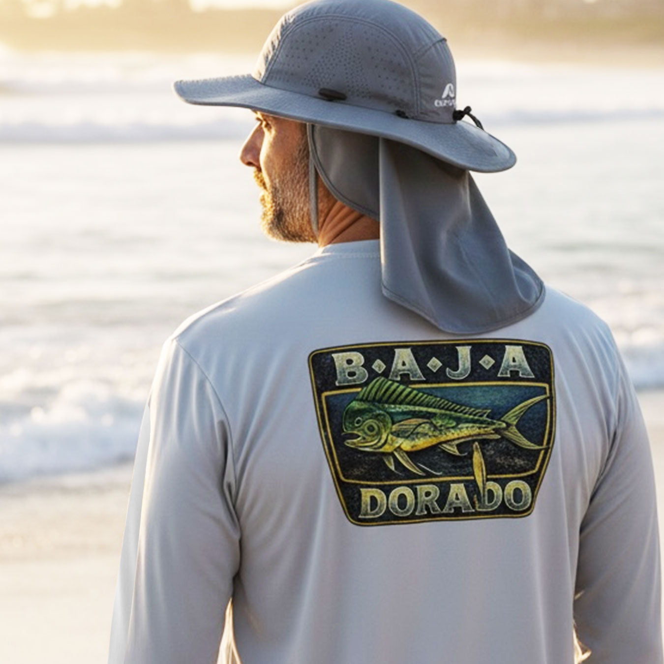 Man wearing a gray cap and shirt with a Baja Dorado logo on a beach.