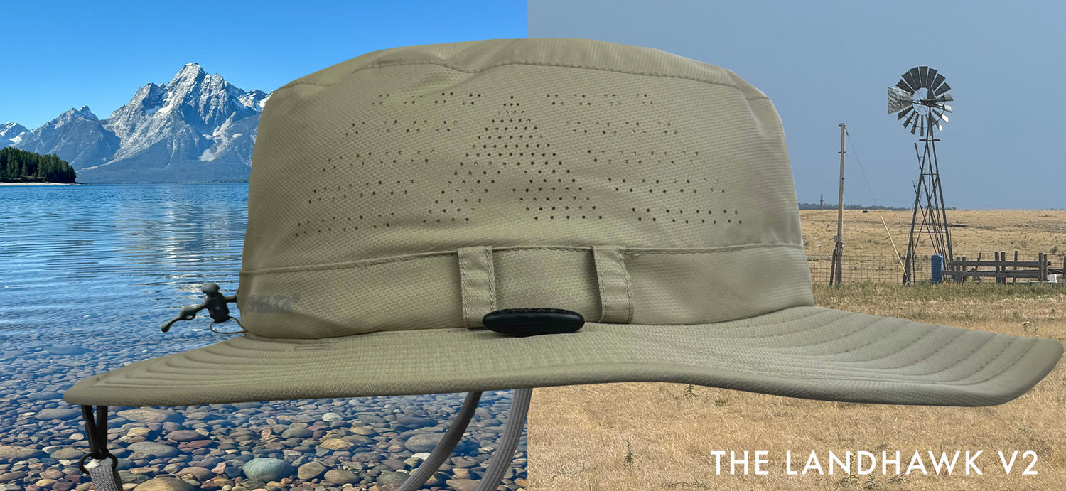 Tan cap with wide brim on a stand against a scenic background of mountains and water.
