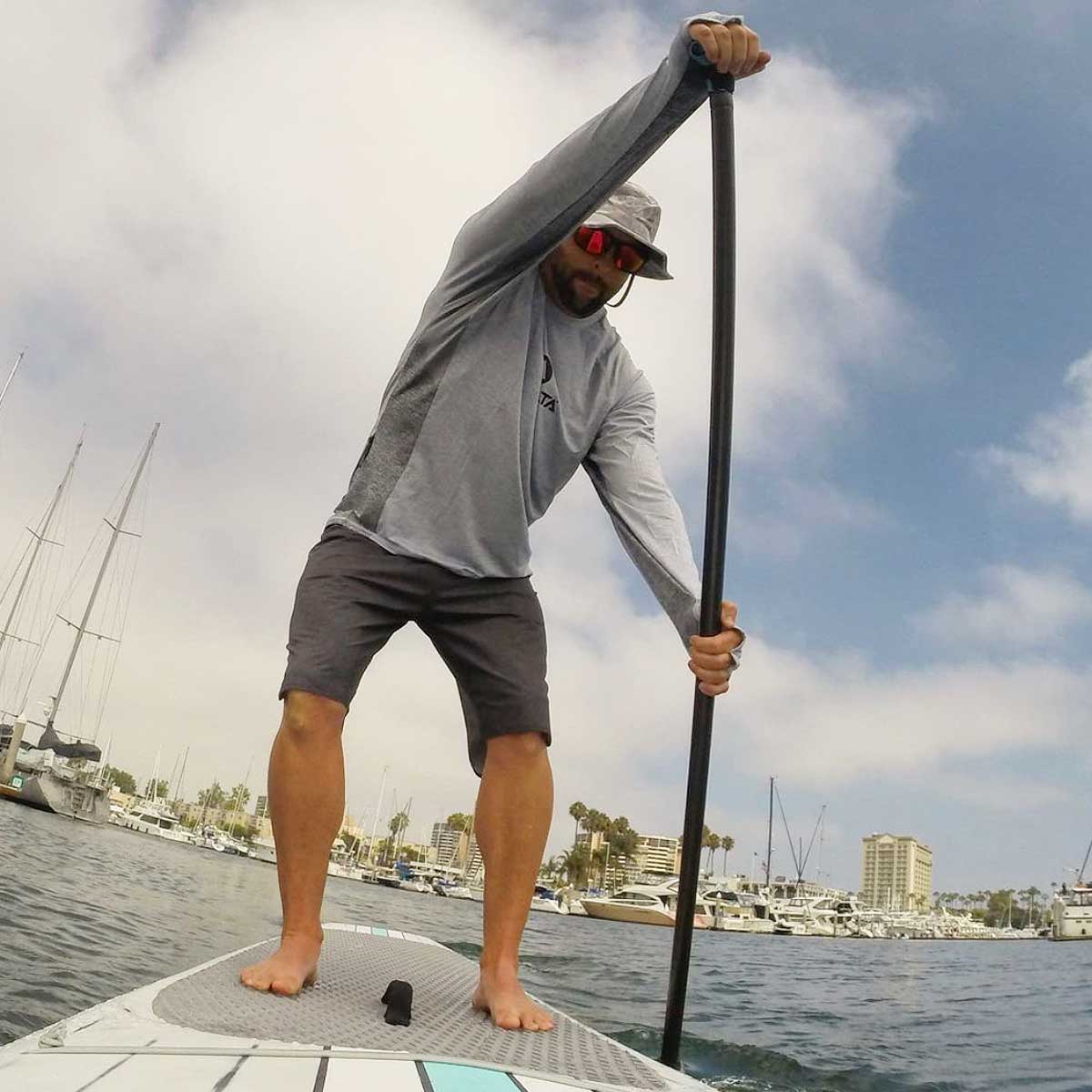 a man stand up paddleboarding wearing a shelta sun hat and sun shirt