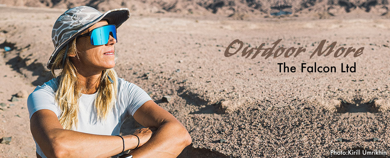 Woman in sunglasses and cap standing on sandy ground with 'Outdoor More The Falcon Ltd' branding.