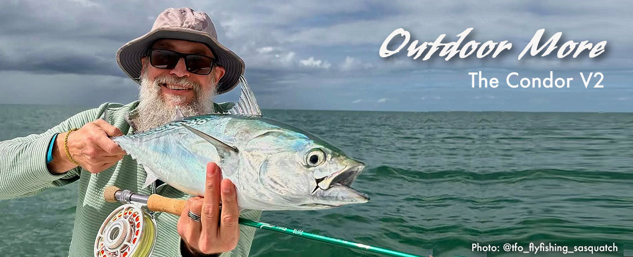 Man holding a large fish with a fishing rod, standing on a beach with 'Outdoor More' and 'The Condor V2' branding.