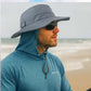 Man wearing a gray wide-brimmed hat and sunglasses on a beach.