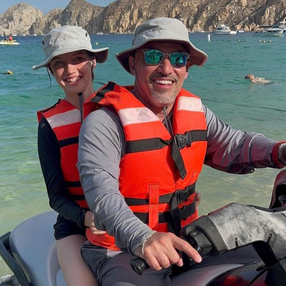 a father and his daughter wearing shelta sun hats while riding a jet ski
