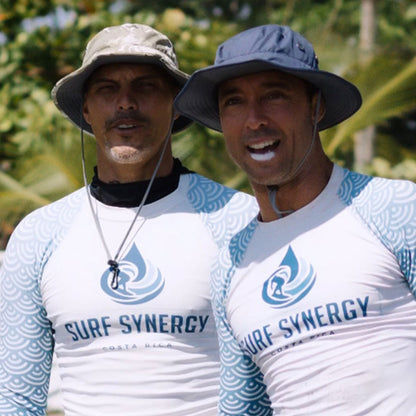 two surfers in rashguards and shelta hats observing a surf contest