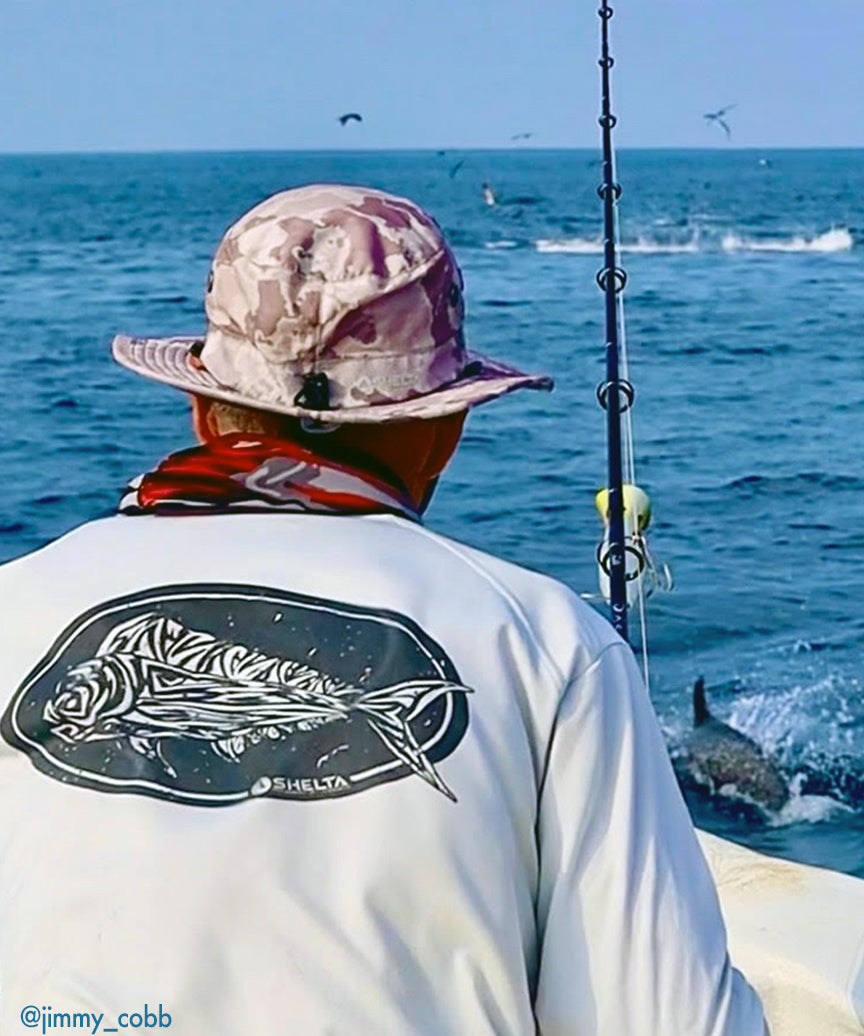 Picture of Man fishing while wearing a shelta shirt and sun hat. Active birds and  fish  in background